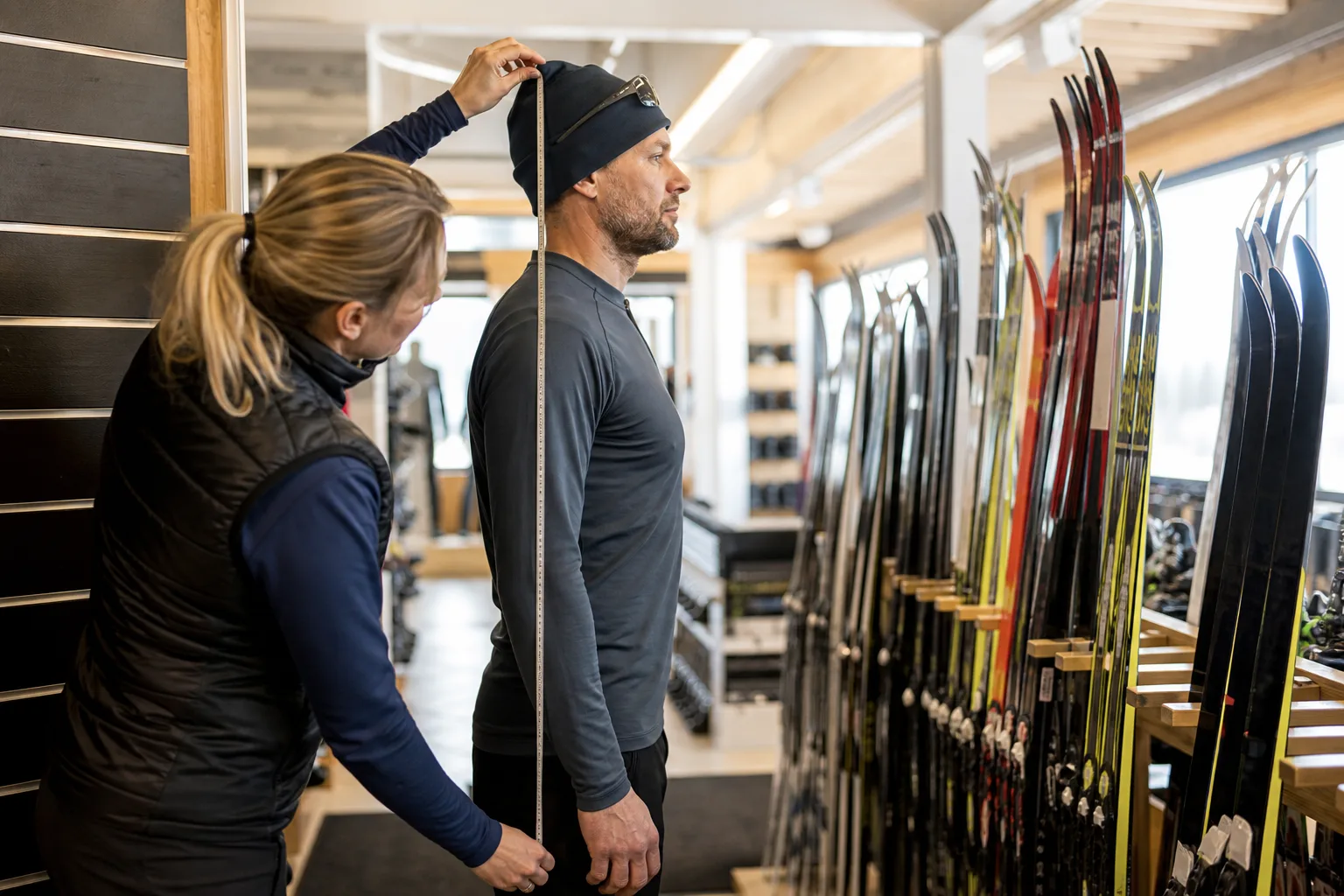 Skidbutikspersonal mäter en kunds kroppslängd inför val av längdskidor