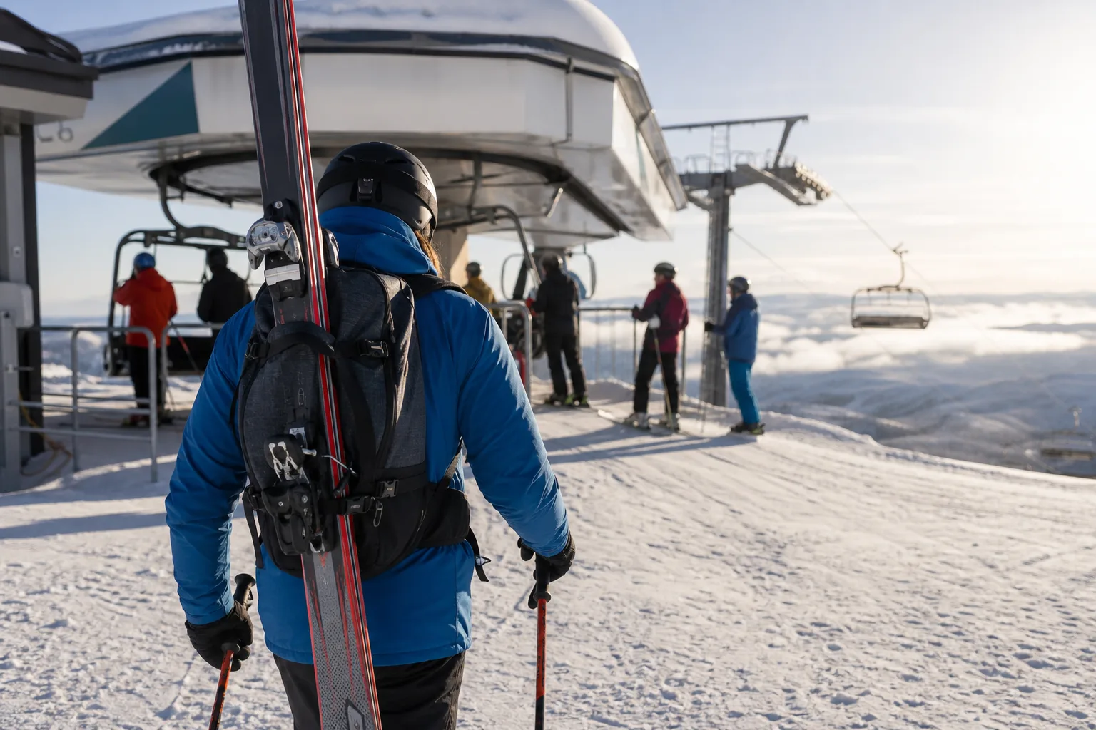 Skidåkare med enkel dagsryggsäck vid en liftstation en solig vinterdag