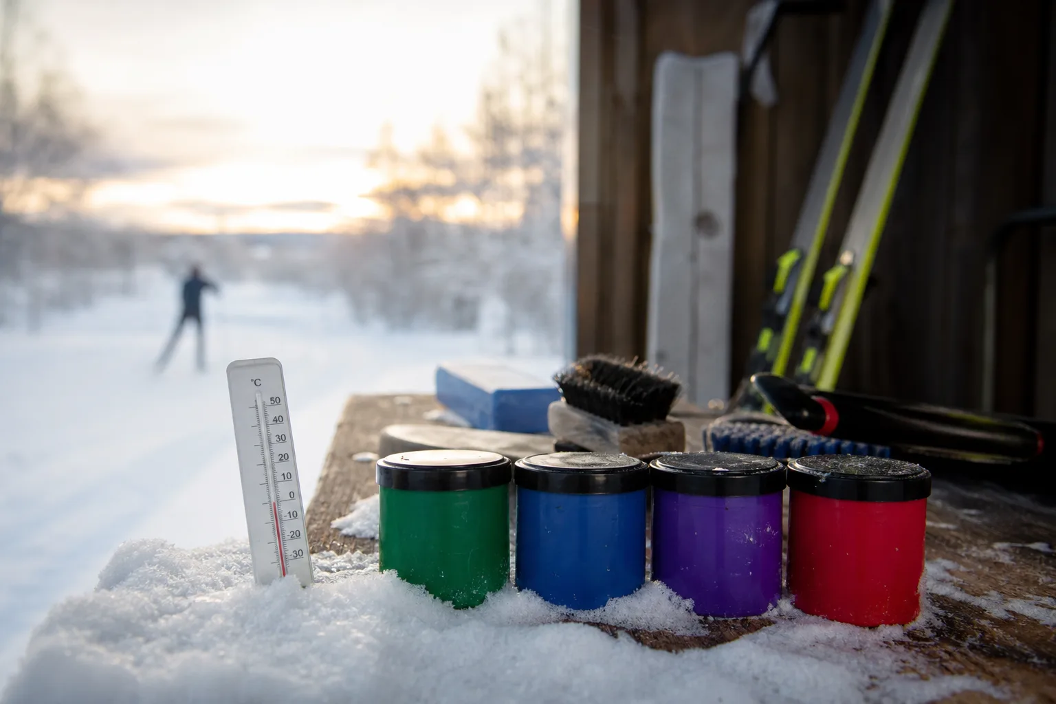 Termometer i snö bredvid färgmärkta vallaburkar i grönt, blått, violett och rött